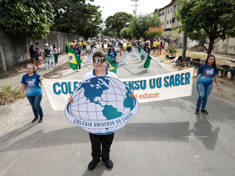 Aluno segurando o globo do colégio à frente da faixa do Colégio Universo do Saber, abrindo o desfile cívico