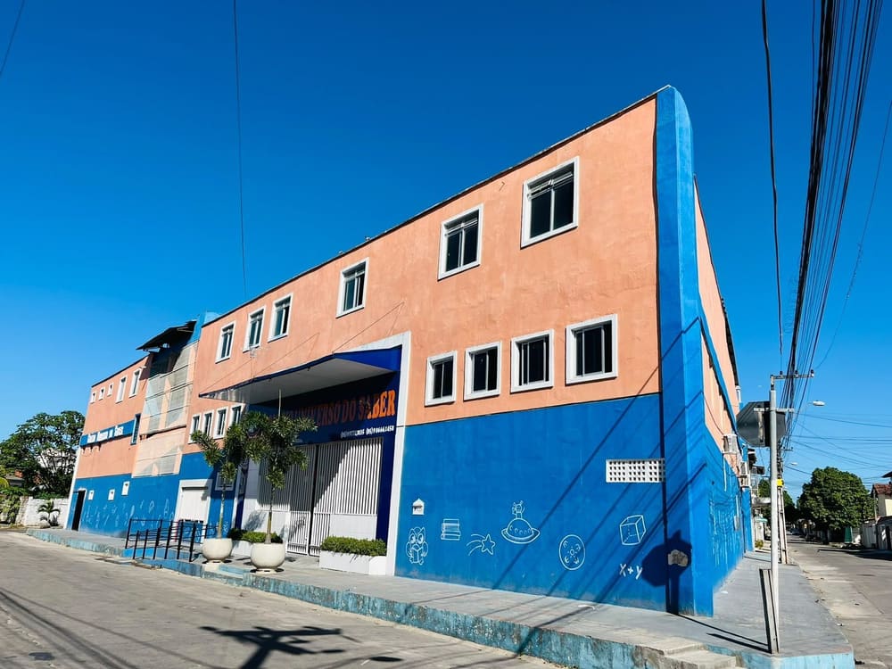 Prédio do Colégio Universo do Saber, azul e salmão, na esquina, num dia de sol