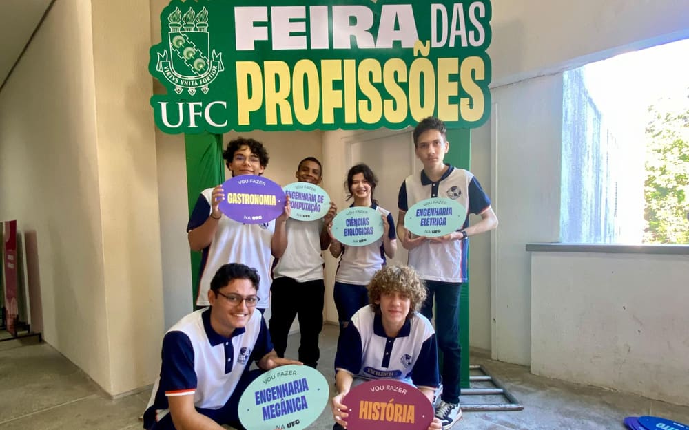 Alunos do colégio na Feira das Profissões da UFC, segurando placas de cursos como Engenharia Mecânica e História