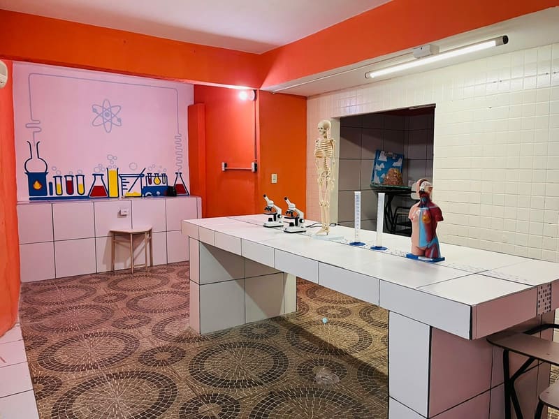 Laboratório de ciências, com a bancada de azulejo, os microscópios e o modelo do corpo humano