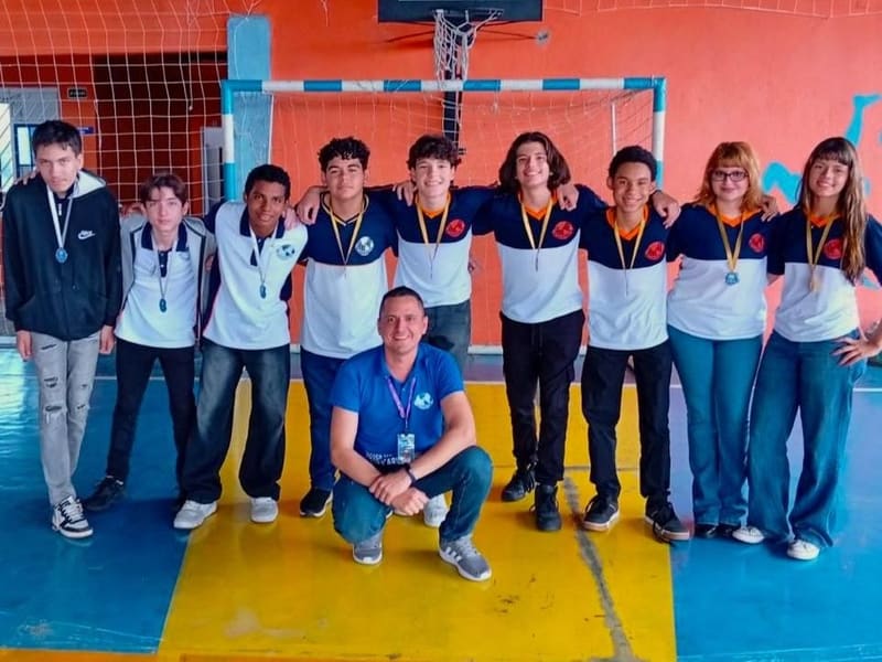 As três equipes medalhistas da Olimpíada Brasileira de Geografia 2026, com as medalhas no pescoço, na quadra do colégio com o professor orientador