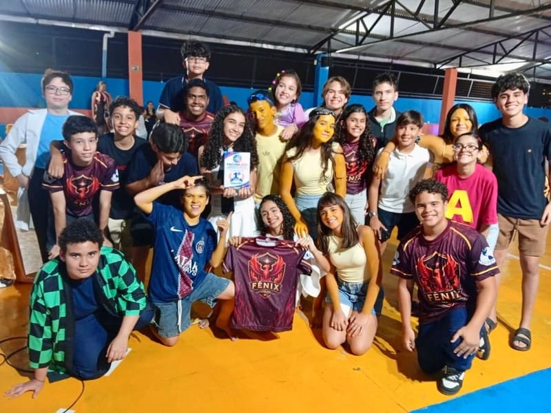 Equipe Fênix comemorando o 1º lugar na FACUSA 2026 com o troféu e a camisa da equipe, na quadra do colégio