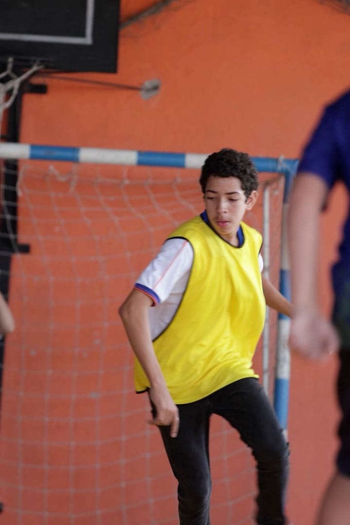 Aluno de colete amarelo prestes a arremessar no handebol